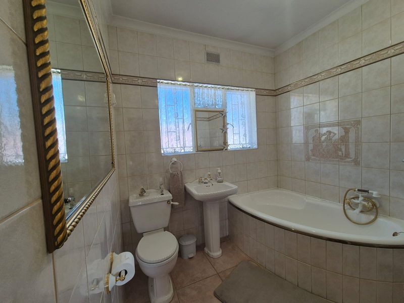 A functional bathroom featuring a pedestal basin, built-in bathtub, and neutral ceramic tiling throughout.