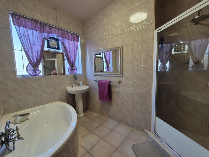 A functional bathroom featuring a corner bathtub, separate shower enclosure, and pedestal basin with neutral wall and floor tiling.