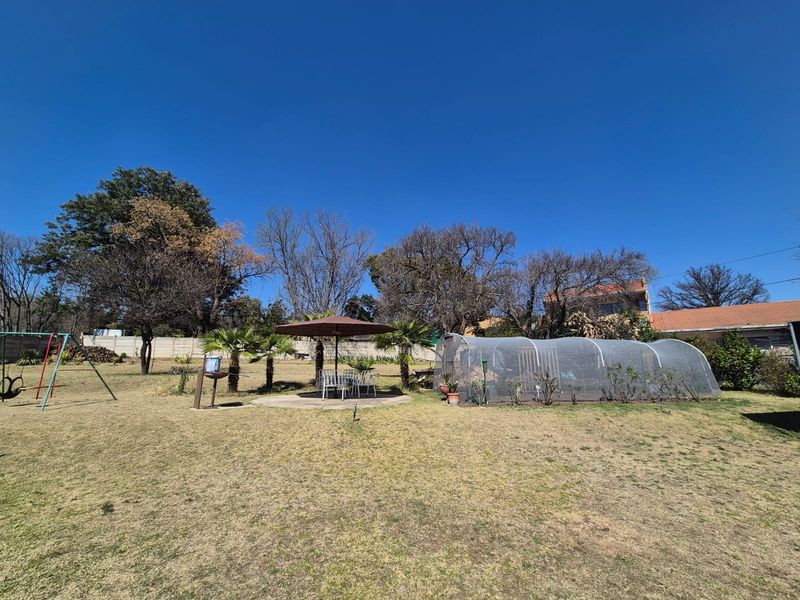 Spacious backyard garden featuring a lawn, a concrete patio area, and a greenhouse structure.