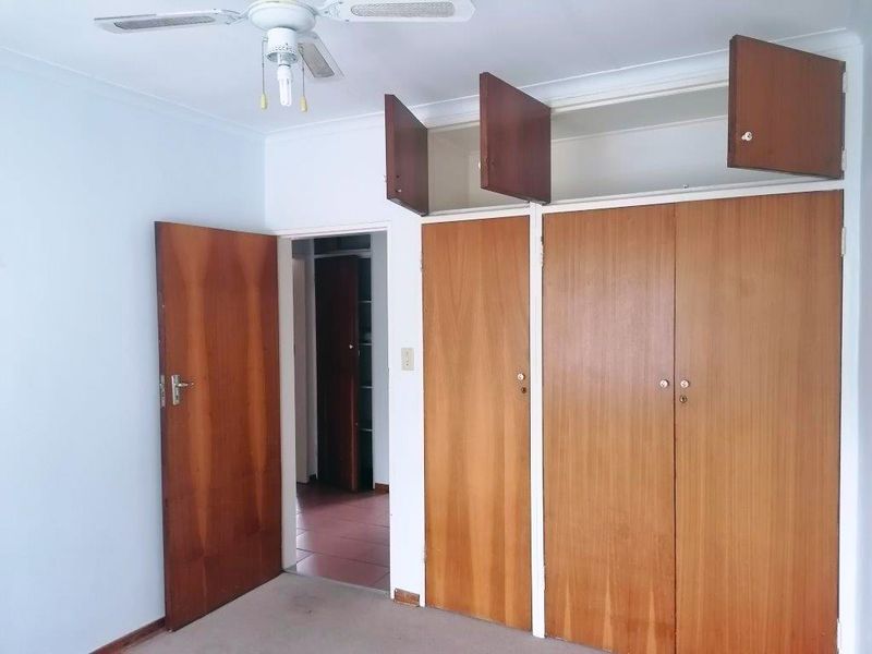 A vacant bedroom featuring built-in wooden cupboards, a ceiling fan, and carpeted flooring, offering a blank canvas for potential updates.