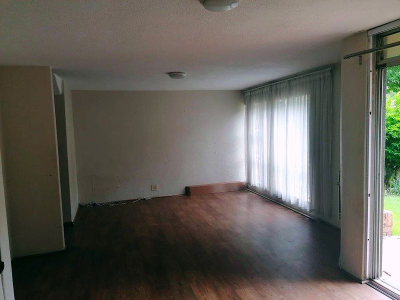 An empty living room featuring laminate flooring and a large sliding glass door providing access to the garden area.