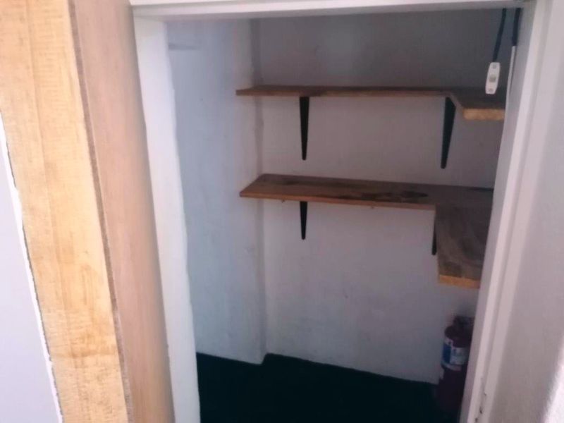 A small storage or pantry area featuring built-in wooden shelving and an unfinished door frame.