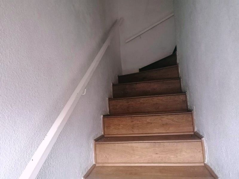 A narrow interior staircase featuring wooden treads and a simple handrail, showing signs of wear on the walls and steps.