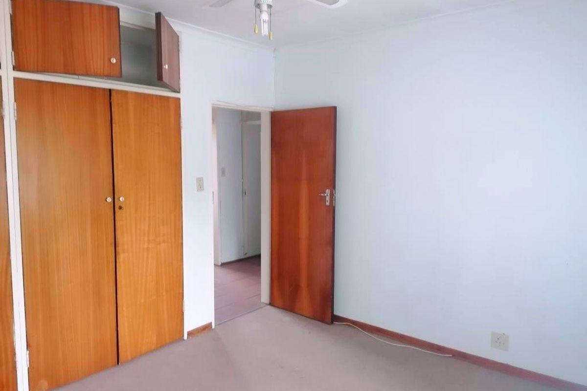 An empty bedroom featuring built-in wooden cupboards, a ceiling fan, and carpeted flooring, offering a blank canvas for renovation or restyling.