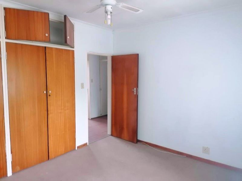 An empty bedroom featuring built-in wooden cupboards, a ceiling fan, and carpeted flooring, offering a blank canvas for renovation or restyling.