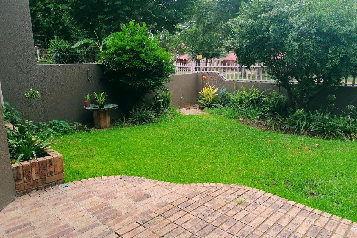 A private rear garden featuring a brick-paved patio, a small lawn, and established perimeter landscaping with a brick planter box.