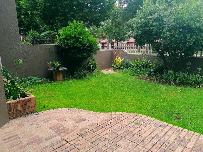 A private rear garden featuring a brick-paved patio, a small lawn, and established perimeter landscaping with a brick planter box.