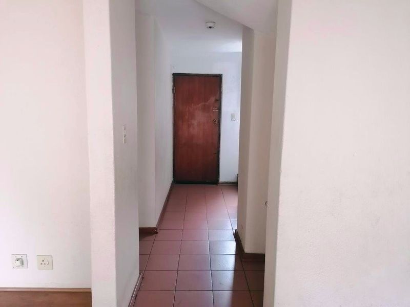A simple, empty hallway featuring tiled flooring and a wooden door, providing access between rooms in the townhouse.