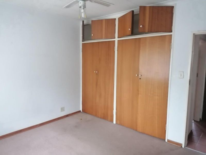 A vacant bedroom featuring built-in wooden cupboards, a ceiling fan, and carpeted flooring, offering a blank canvas for potential updates.