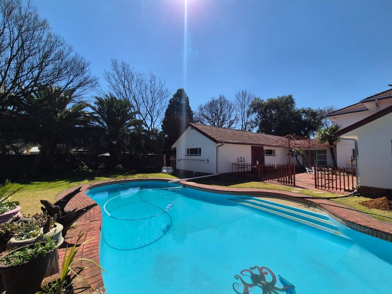 A backyard pool area featuring a curved swimming pool with brick coping, adjacent tiled patio space, and established garden surroundings.