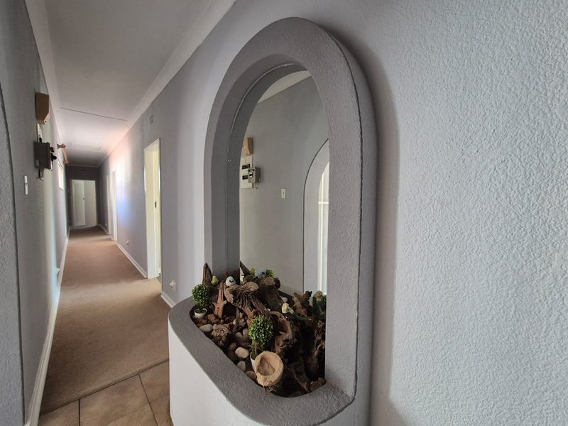 A well-lit hallway featuring a unique built-in arched display niche, coved ceiling cornices, and a combination of tiled and carpeted flooring.