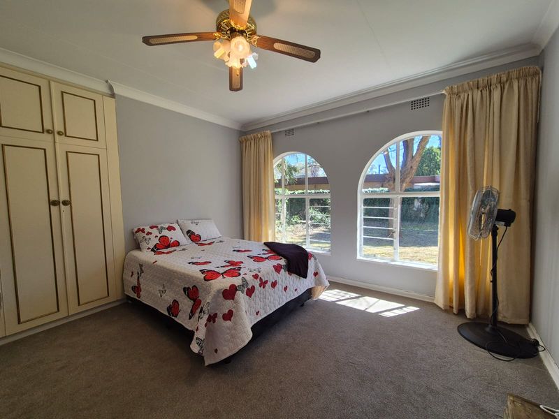 Spacious bedroom featuring built-in cupboards, carpeted flooring, and distinctive arched windows that provide natural light and garden views.