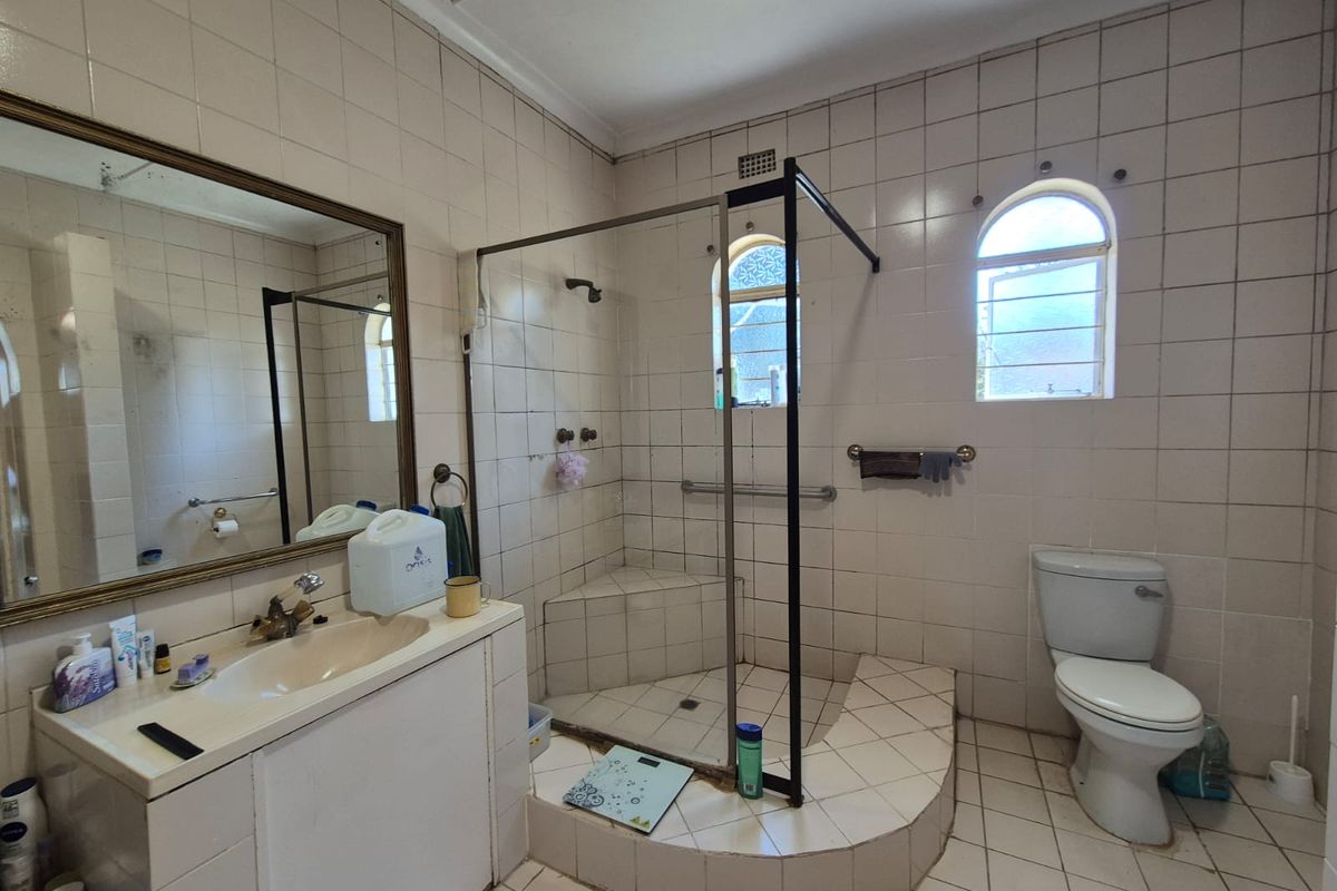 A dated bathroom featuring a walk-in shower with a raised base, built-in vanity, and tiled finishes, offering potential for a modern renovation.
