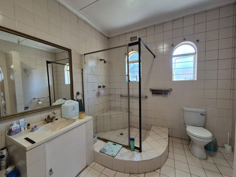 A dated bathroom featuring a walk-in shower with a raised base, built-in vanity, and tiled finishes, offering potential for a modern renovation.