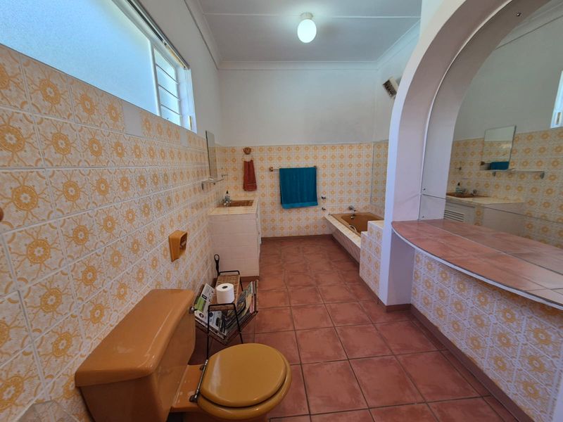A spacious, vintage-style bathroom featuring original tiled walls, a built-in bathtub, and a tiled vanity area with a large mirror.