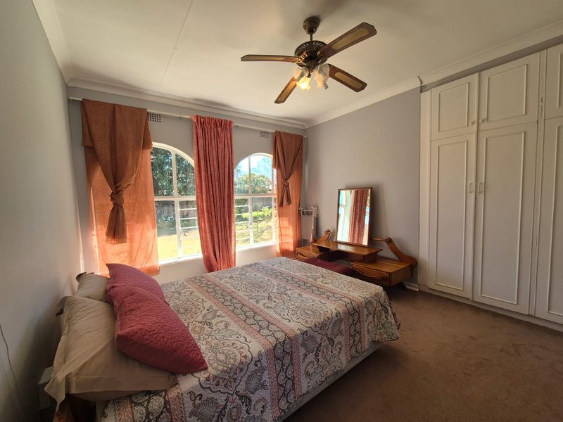 A bedroom featuring built-in wardrobes, a ceiling fan, and arched windows that provide natural light.