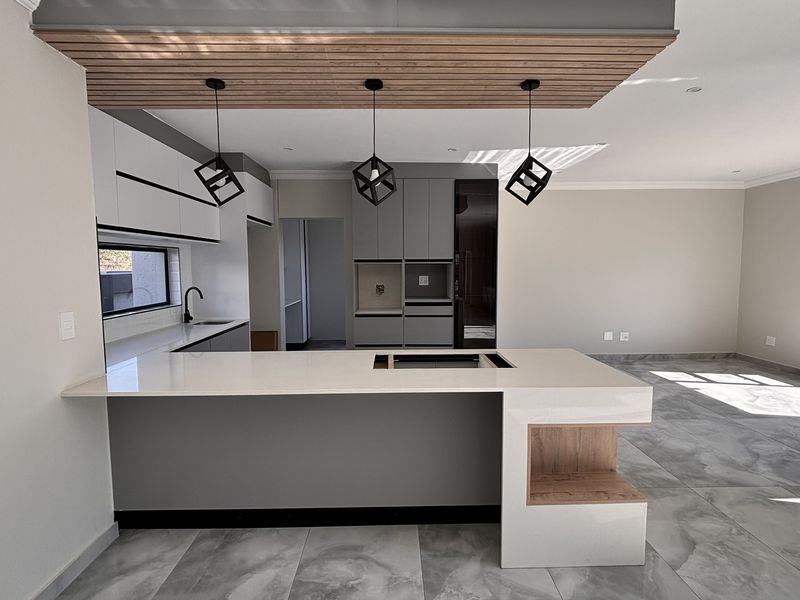 Modern open-plan kitchen featuring a large island with quartz countertops, sleek cabinetry, and a stylish timber slat ceiling detail in a bright, spacious area.