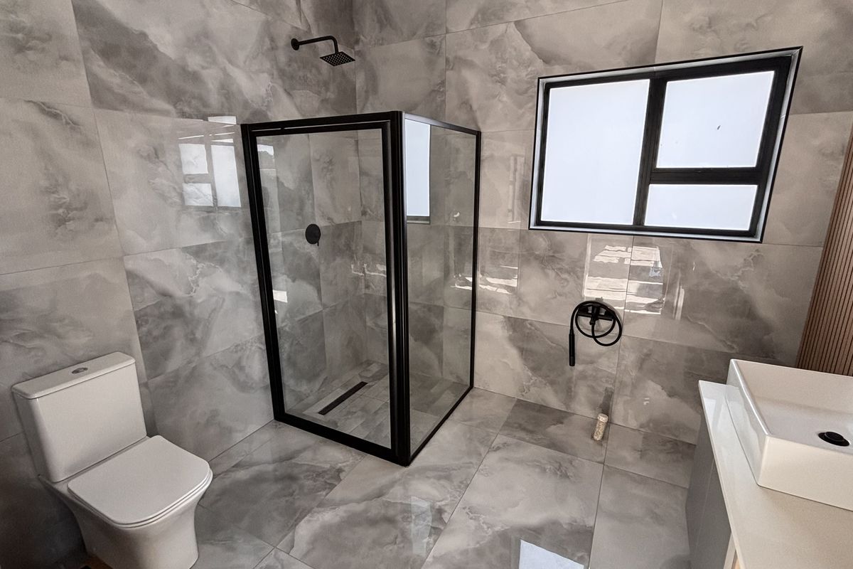 Modern bathroom featuring large-format grey marble-look tiles, a walk-in shower with black frame, and a contemporary vanity basin.