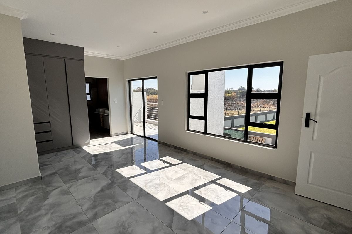 A bright, modern, and spacious bedroom featuring polished tiled floors, built-in cupboards, and large windows with access to an outdoor balcony area.
