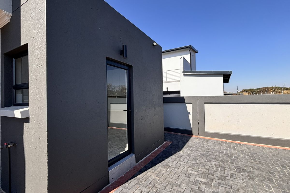 A modern rear exterior area featuring a paved patio, dark grey rendered walls, and a secure boundary wall under a clear blue sky.