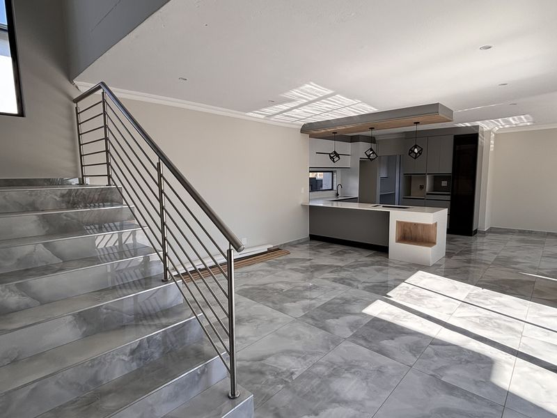 Modern open-plan living area featuring high-gloss marble-look floor tiles, a sleek kitchen island, and a contemporary staircase with stainless steel railings.