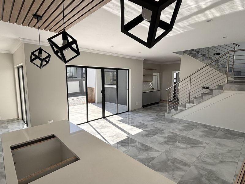 Spacious open-plan living area featuring modern marble-look floor tiles, a striking timber slat ceiling detail, and a contemporary staircase with stainless steel railings.