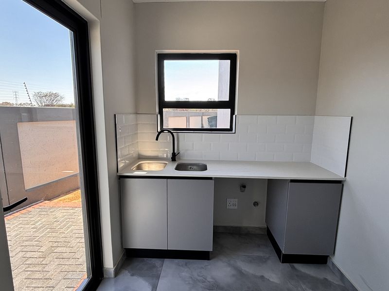 A clean, modern scullery featuring built-in cabinetry, a stainless steel sink with a black mixer tap, and a subway tile backsplash.