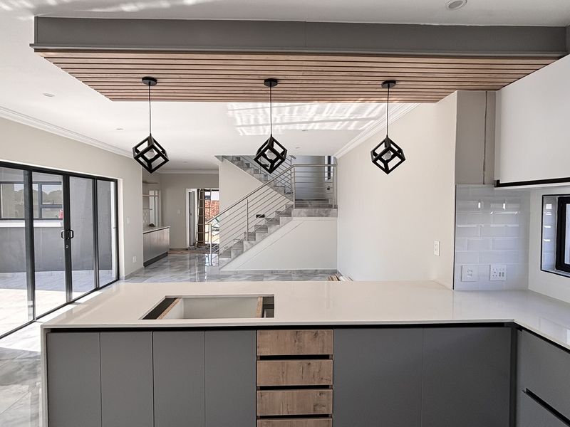 Modern open-plan kitchen and living area featuring a central island, timber slat ceiling detail, and a sleek staircase leading to the upper level.