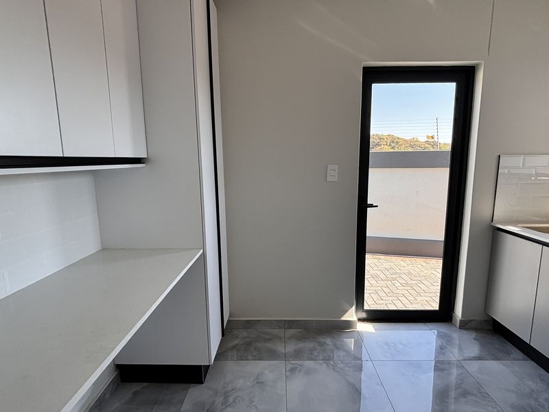 A modern, clean scullery featuring white built-in cabinetry, stone countertops, subway tile backsplash, and direct access to an outdoor patio area.