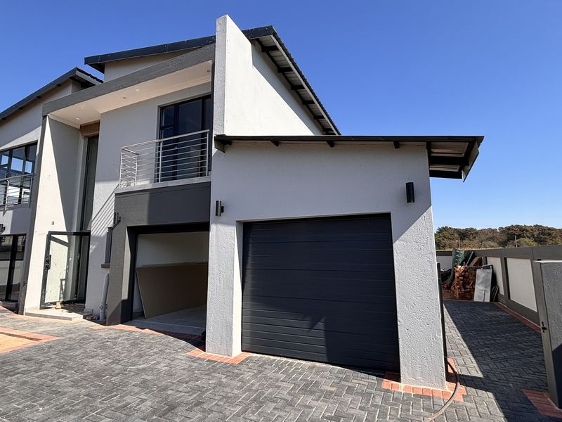 Front elevation of a modern double-story house featuring a garage, paved driveway, and a balcony with metal balustrades.