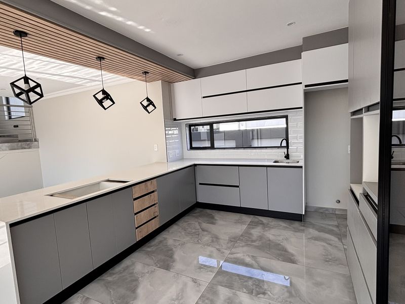 Modern kitchen featuring sleek grey and white cabinetry, stone countertops, subway tile backsplash, and a unique slatted timber ceiling detail with pendant lighting.