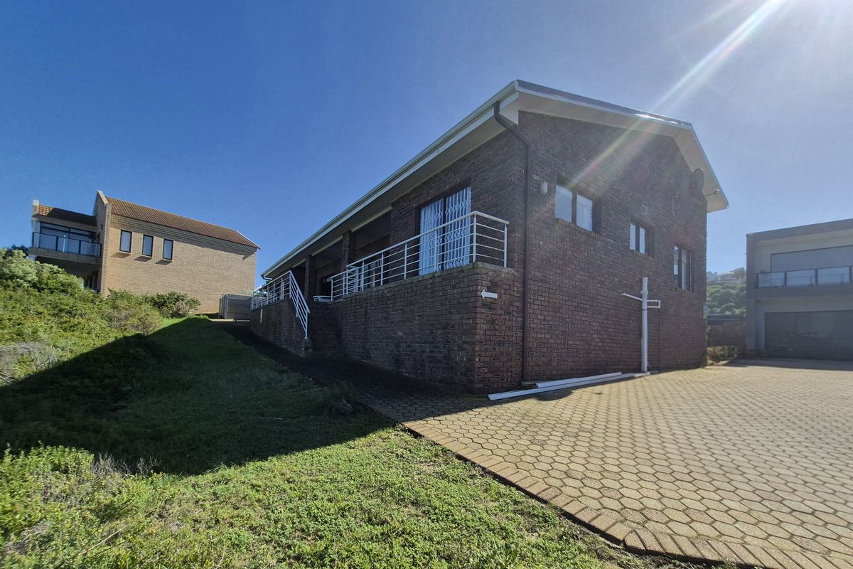 Rear view of a brick house featuring a paved driveway, elevated balcony with metal railings, and security gates.