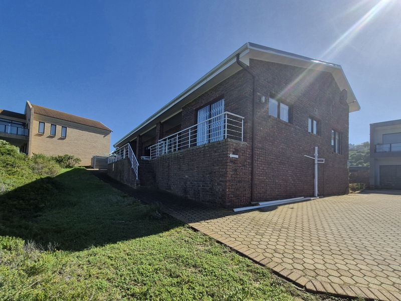Rear view of a brick house featuring a paved driveway, elevated balcony with metal railings, and security gates.