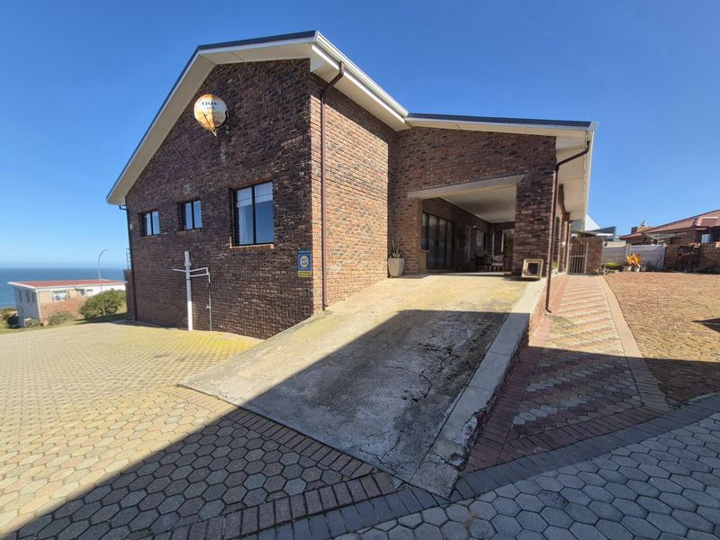 Front exterior view of a face brick house featuring a paved driveway, a concrete ramp leading to a covered entrance, and coastal views.