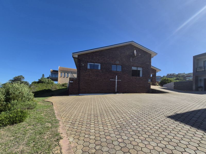 A view of the front brick facade and paved driveway of the property under a clear blue sky.