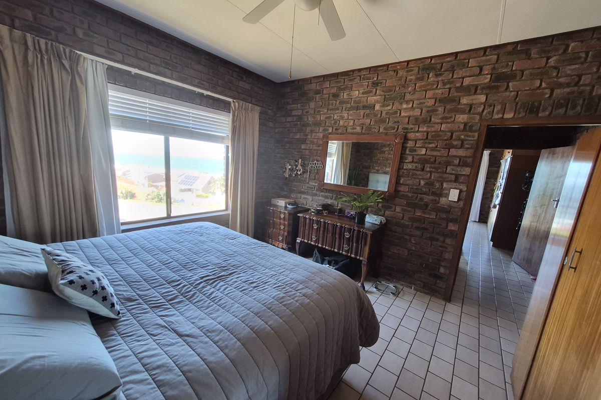 A bedroom featuring exposed brick walls, tiled flooring, a ceiling fan, and built-in cupboards, with a window offering a view.