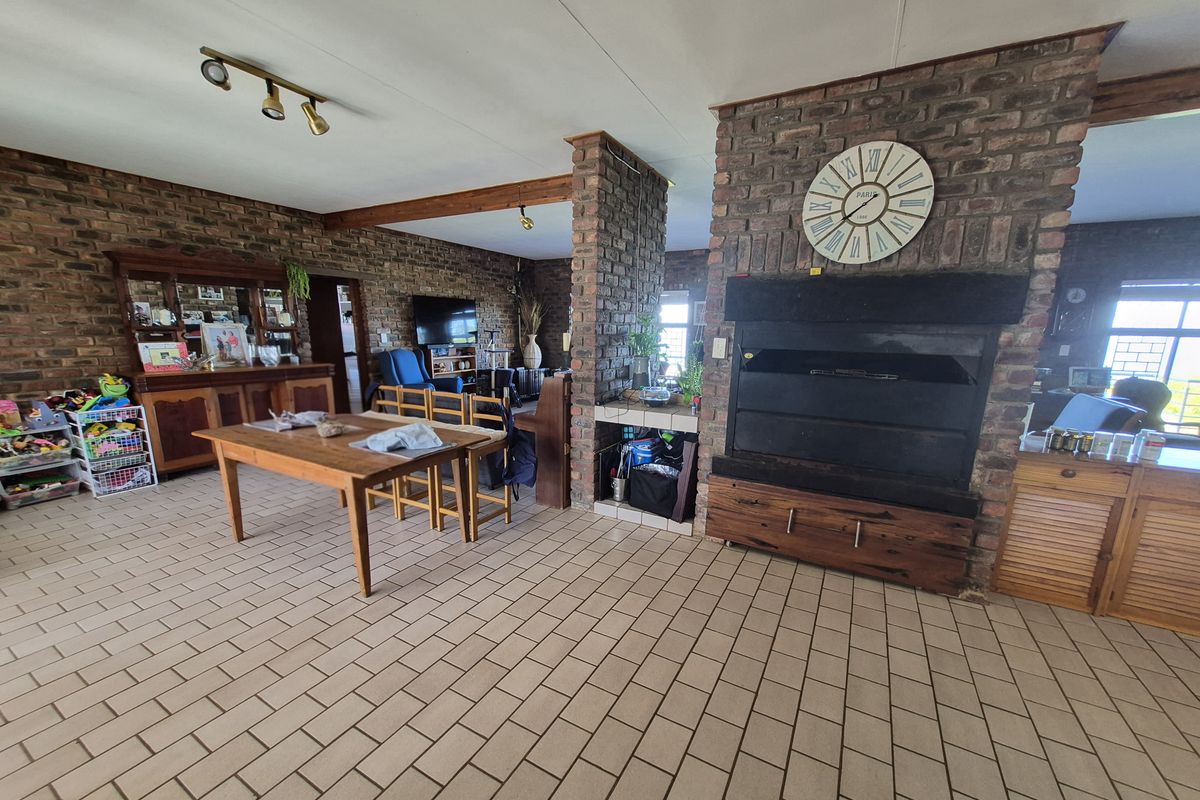 Spacious living area featuring exposed brick walls, a large built-in fireplace, and tiled flooring with exposed timber ceiling beams.