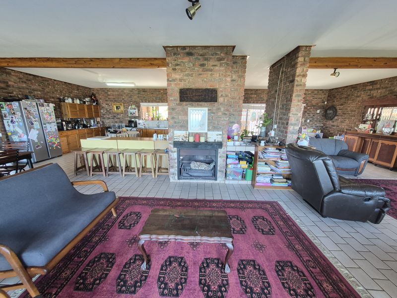 Spacious open-plan living and kitchen area featuring a central brick fireplace, exposed timber beams, and tiled flooring throughout.