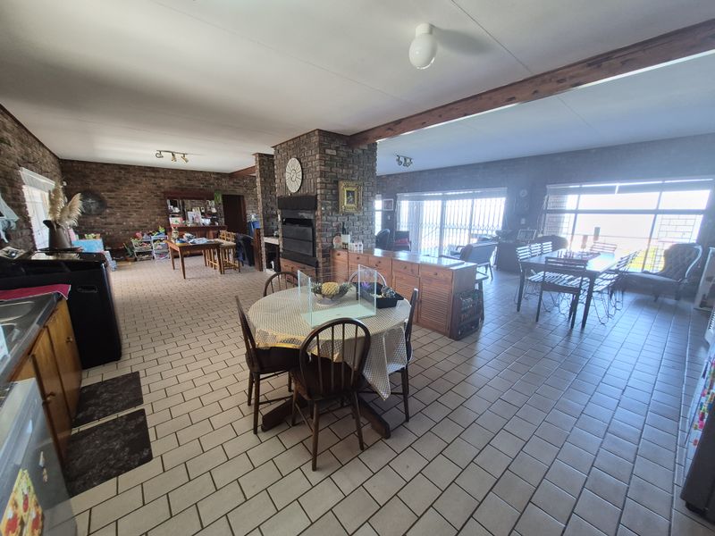 Spacious open-plan living and dining area featuring exposed brickwork, timber ceiling beams, tiled flooring, and large sliding doors leading to the exterior.