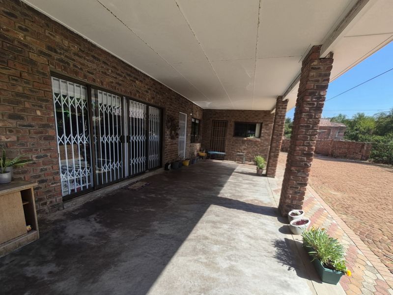 A spacious covered patio area featuring exposed brickwork, concrete flooring, and secure metal gates, offering a functional outdoor living space.