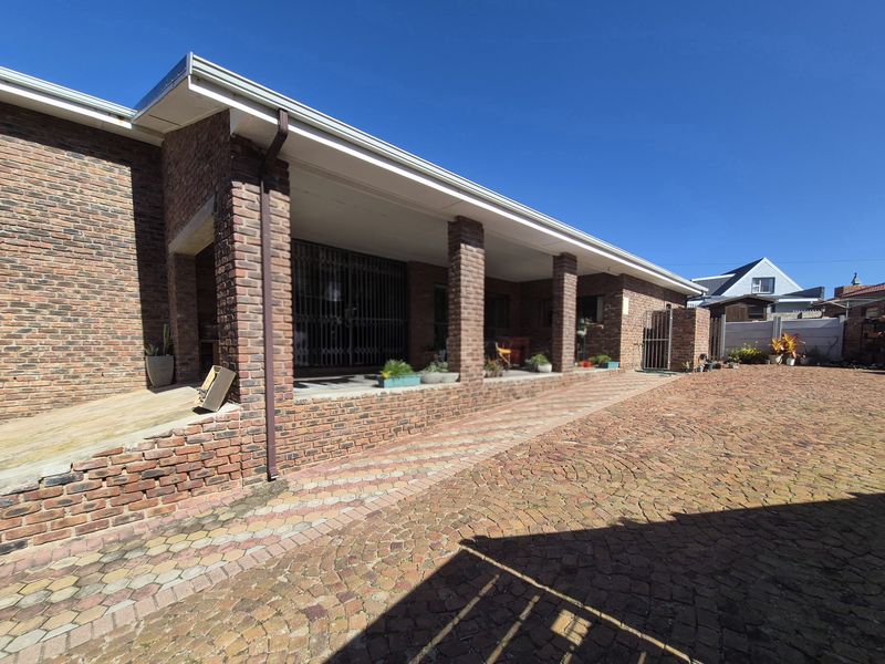 A spacious rear exterior view featuring a covered patio area, brick facade, and extensive paved courtyard space.