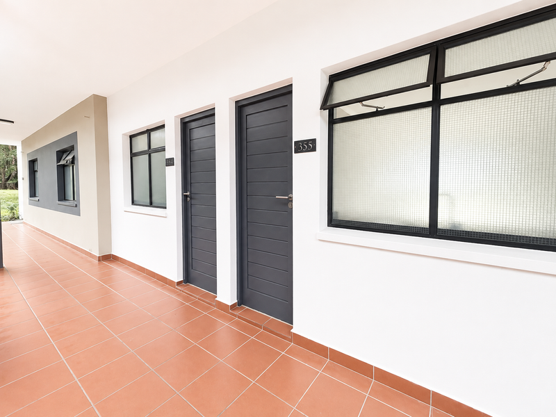 A clean, well-maintained exterior hallway featuring tiled flooring, dark grey doors, and modern awning windows with security glass.
