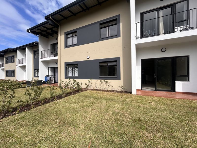 Rear view of a modern apartment complex featuring ground floor patios, upper-level balconies, and a well-maintained communal garden area.