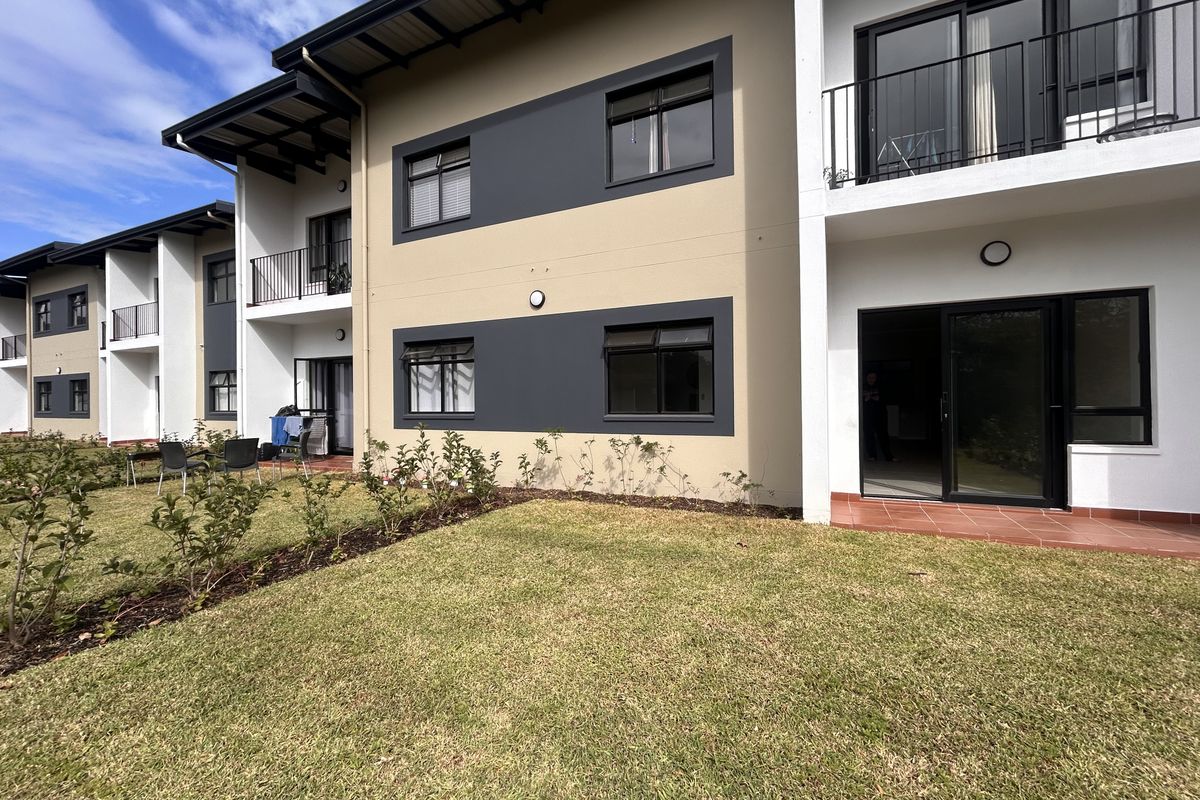 Rear view of a modern apartment complex featuring ground floor patios, upper-level balconies, and a well-maintained communal garden area.