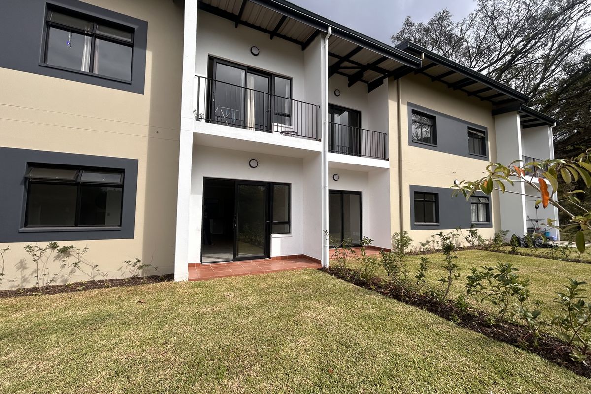 Rear view of a modern apartment building featuring ground floor patios, upper-level balconies with metal railings, and well-maintained garden space.