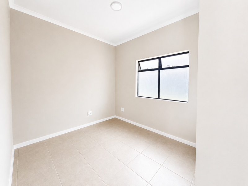 A clean, empty bedroom featuring neutral wall paint, tiled flooring, and an aluminium-framed window with obscured glass.
