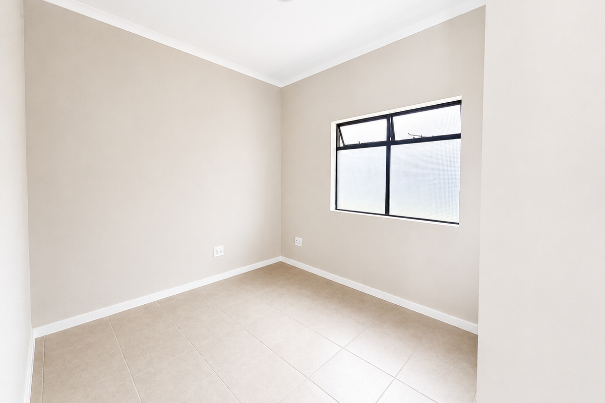 A clean, empty bedroom featuring neutral wall paint, tiled flooring, and an aluminium-framed window with obscured glass.