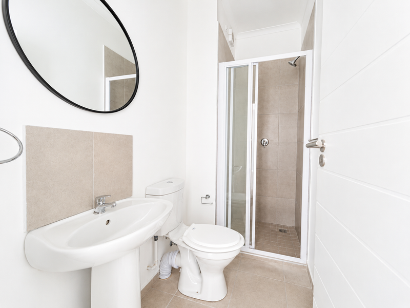 A clean, modern bathroom featuring a pedestal basin, toilet, and a separate shower enclosure with neutral tiling.