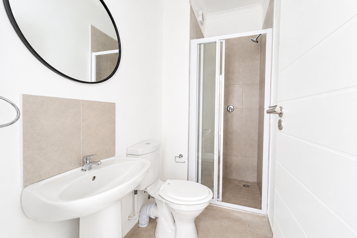 A clean, modern bathroom featuring a pedestal basin, toilet, and a separate shower enclosure with neutral tiling.