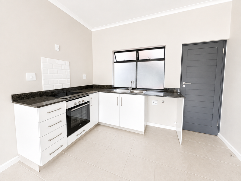 A clean, modern kitchen featuring white cabinetry, granite countertops, a built-in oven and hob, and a subway tile splashback in a neutral, well-lit space.